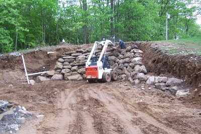Skid steer with pallet forks building stone wall